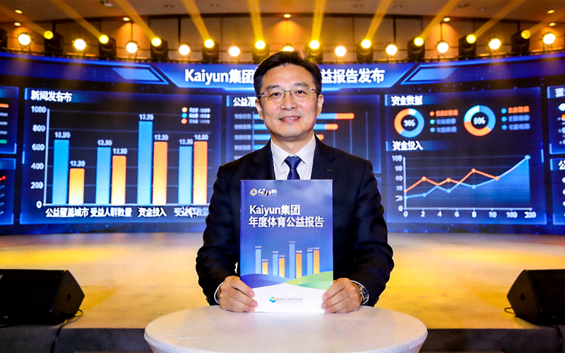 Kaiyun集团年度体育公益报告发布会现场 - 集团高管在台上展示报告内容，背景是巨大的屏幕显示着公益数据图表
