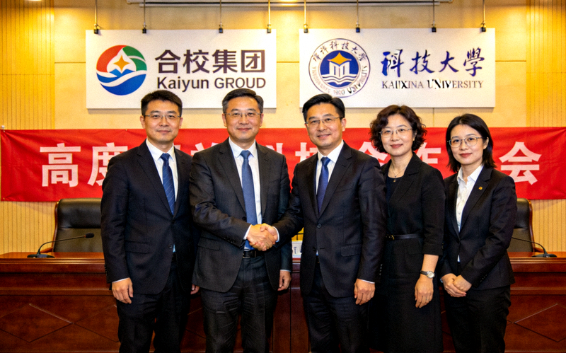 Kaiyun集团与高校战略合作签约仪式 - 双方代表在礼堂内握手合影，背景是合作项目的标志和高校校徽